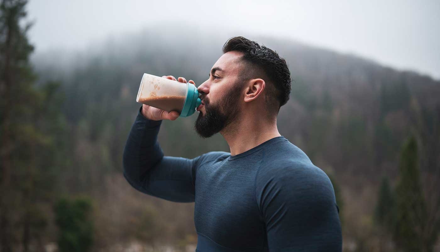 Muškarac pije proteinski shake na otvorenome.
